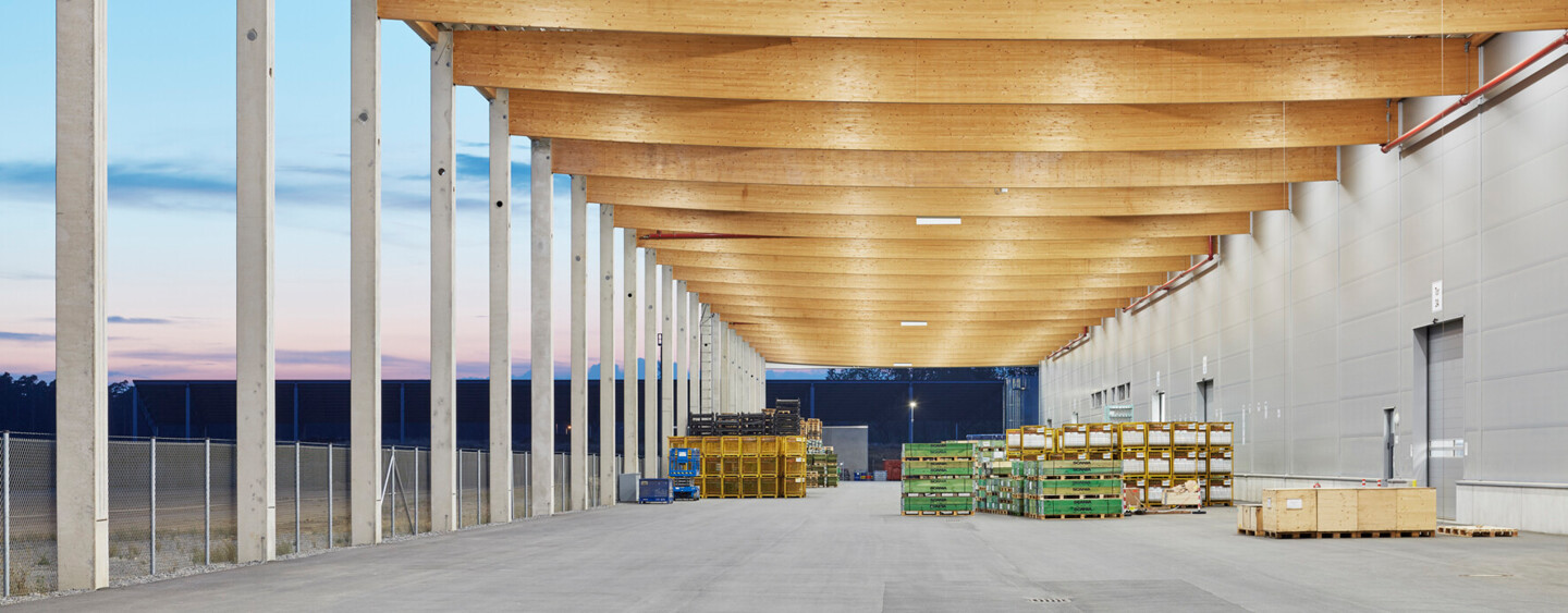 Das Holztragwerk mit Fischbauchbindern setzt sich im Außenbereich fort. Die außergewöhnlich großen Vordächer ermöglichen eine witterungsunabhängige Lagerung und Verladung.