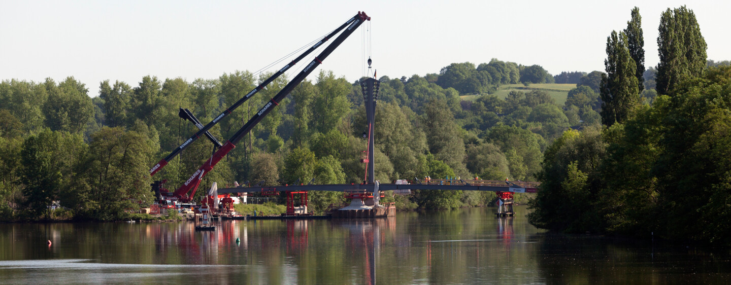 Die Seilpylone der neuen Kampmannbrücke in Essen werden vor der idyllischen Kulisse der Ruhr versetzt.